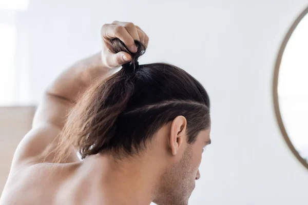 back view of man styling long hair in bun