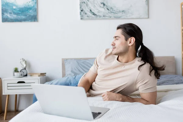 Freelancer Con Pelo Largo Acostado Cama Cerca Del Ordenador Portátil — Foto de Stock