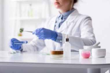 Bulanık lateks eldivenli laboratuvar asistanının yanında kozmetik ürünleri olan kaplar. 