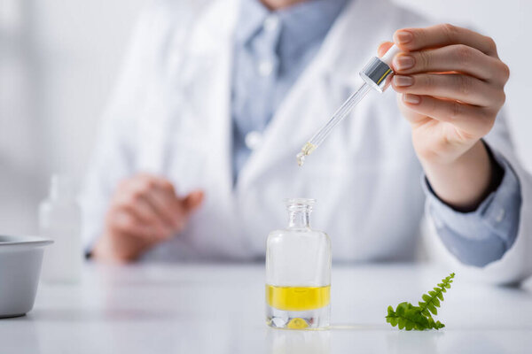 fern leaves near laboratory assistant holding pipette above bottle with serum