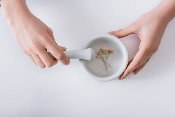 top view of woman grinding dried flowers in mortar with pestle on white
