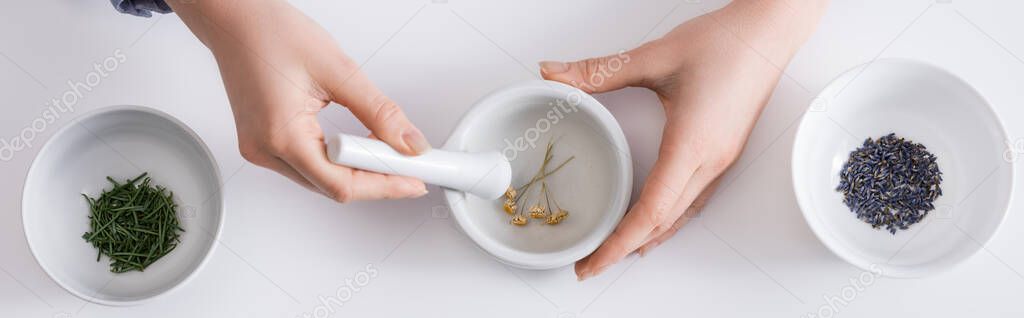 top view of woman grinding dried flowers in mortar with pestle on white, banner