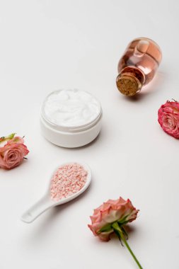 Pembe deniz tuzuna yakın çiçekler, gül suyuyla dolu bir şişe ve beyaz kremalı bir kap.