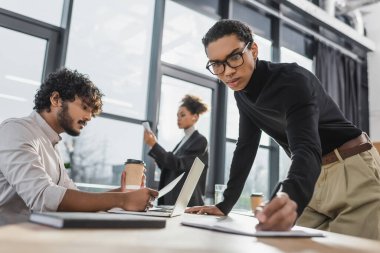Afrikalı Amerikalı iş adamı, Hindistan 'daki meslektaşının yanında, ofisinde kağıt ile deftere yazı yazıyor. 