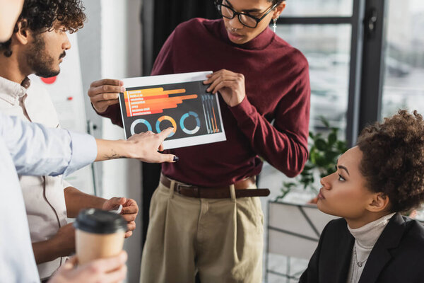 African american businessman holding paper with graphs near interracial colleagues in office 