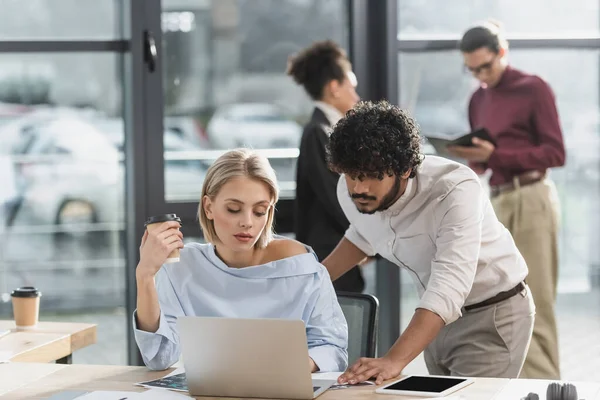 Businesswoman Holding Takeaway Drink While Using Laptop Indian Colleague Office — Stock Photo, Image