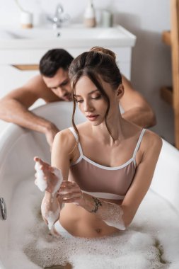Esmer kadın evde bulanık erkek arkadaşının yanında banyo yaparken köpüklü ellere dokunuyor. 