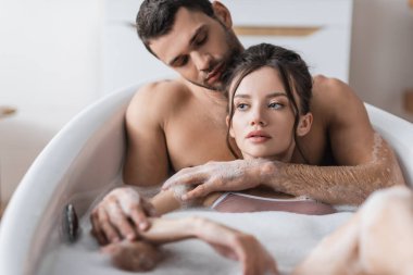 Kaslı adam evde banyo yaparken kız arkadaşına sarılıyor. 