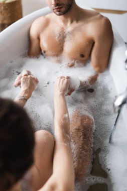 Banyo küvetinde köpükle el ele tutuşan bulanık çift görüntüsü. 