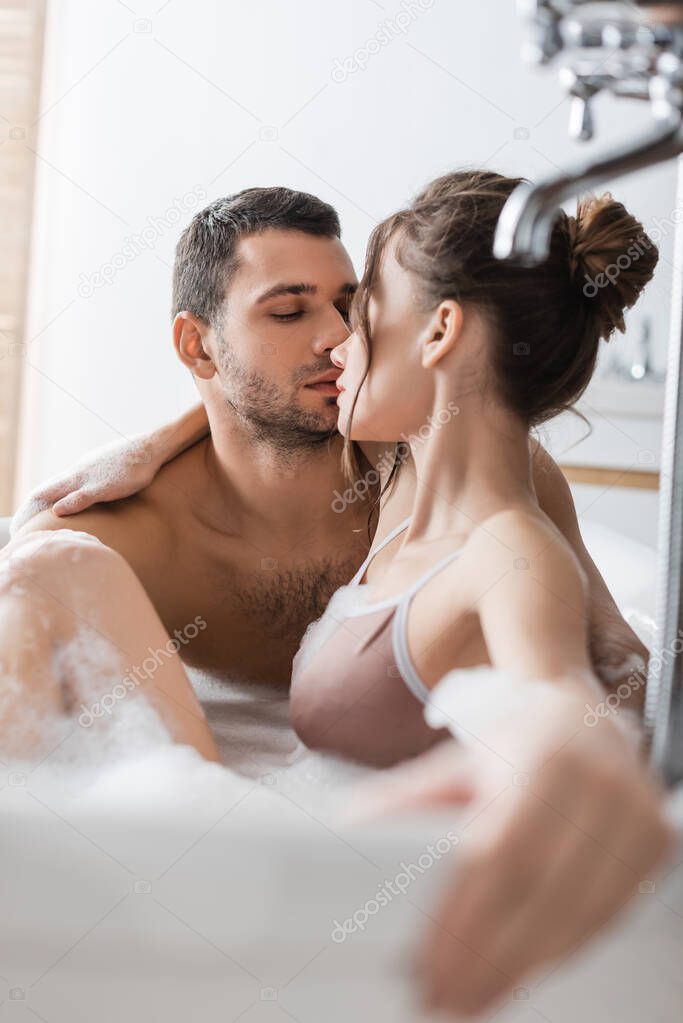 Muscular man kissing brunette girlfriend in bath with foam at home 