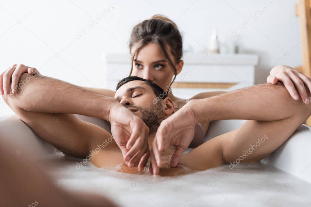 Blurred woman kissing muscular boyfriend in bath at home 