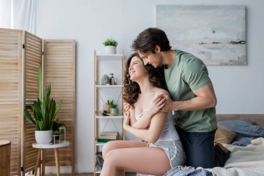 Mutlu adam modern yatak odasında neşeli ve kıvırcık kadına sarılıyor.