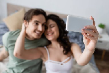 Bulanık ve mutlu çift yatak odasında selfie çekiyor.