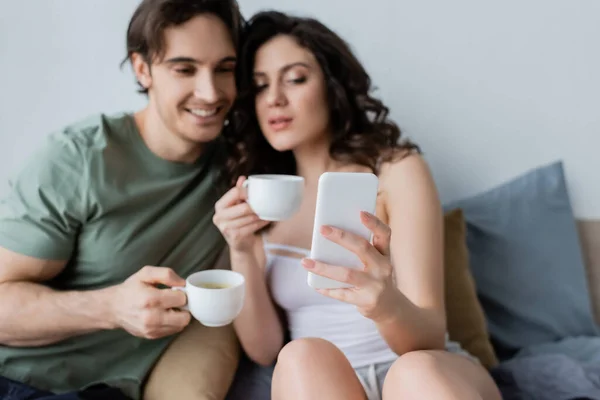 Blurred Couple Cups Looking Smartphone Bedroom — ストック写真