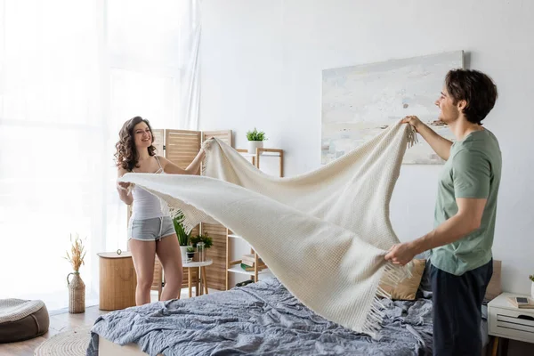 Feliz Joven Pareja Cubriendo Cama Con Manta —  Fotos de Stock