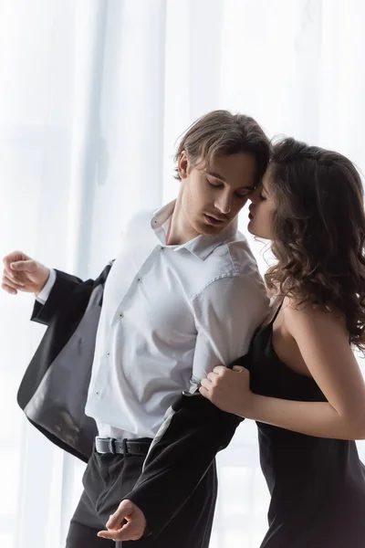 young curly woman in slip dress taking off blazer on boyfriend