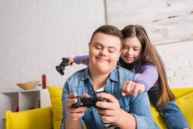 KYIV, UKRAINE - 21 Ocak 2022: Down sendromlu gülümseyen çocuk evinde arkadaşının yanında joystick tutuyor 