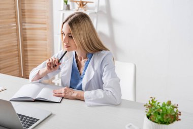 Konuşma terapisti danışma odasında dizüstü bilgisayarın yanında kalem tutuyor. 