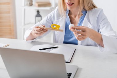 Konuşma terapistinin danışma odasındaki dizüstü bilgisayardaki video görüşmesi sırasında elinde solunum kası eğitmeni tutarken görüntüsü kesilmiş. 