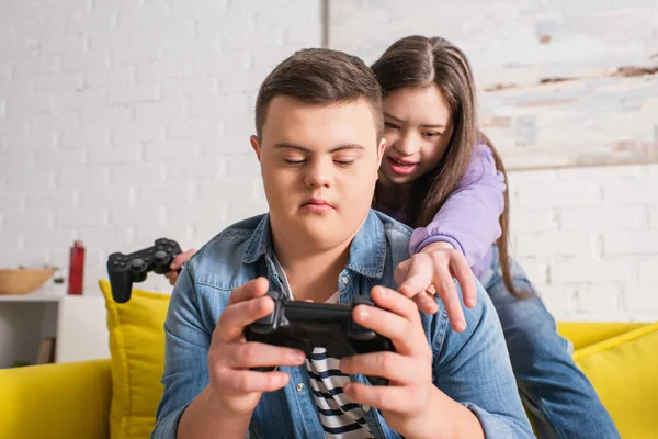 KYIV, UKRAINE - 21 HAZİRAN 2022: Evdeki genç arkadaşının elinde joystick 'i gösteren Down sendromlu kız 