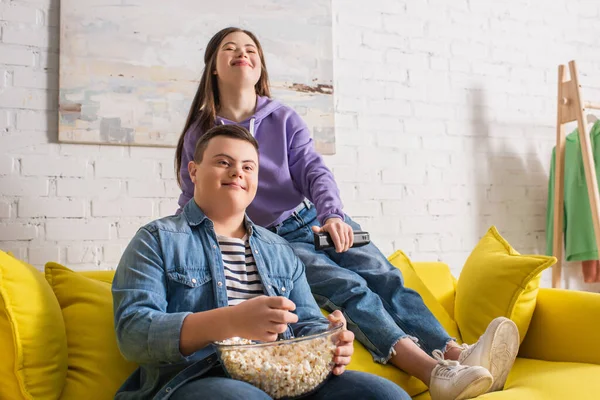Uśmiechnięty Nastolatek Zespołem Downa Trzymający Popcorn Blisko Przyjaciela Zdalnym Sterowaniem — Zdjęcie stockowe