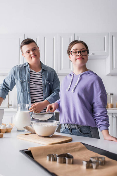 Подростки с синдромом Дауна смотрят в камеру возле еды на кухне 