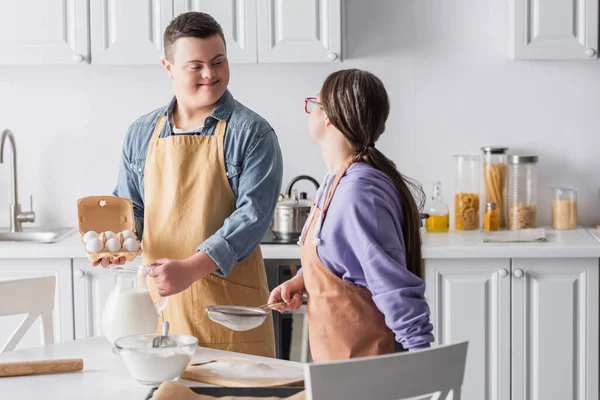 Sonriente Adolescente Con Síndrome Sosteniendo Ingredientes Cerca Novia Delantal Cocina — Foto de Stock