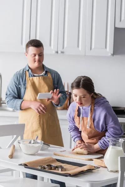 Adolescente Com Síndrome Fazendo Massa Perto Amigo Com Smartphone Cozinha — Fotografia de Stock