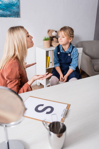 Speech therapist working with child near blurred mirror and letter in consulting room 