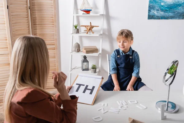 Niño Sonriente Sentado Cerca Del Terapeuta Del Habla Con Portapapeles — Foto de Stock