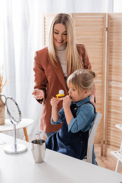 Smiling speech therapist standing near pupil with respiratory muscle trainer in classroom 