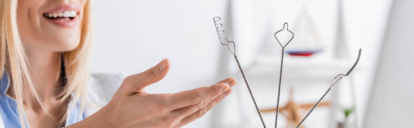 Cropped view of positive logopedist pointing at tools near laptop in consulting room, banner 