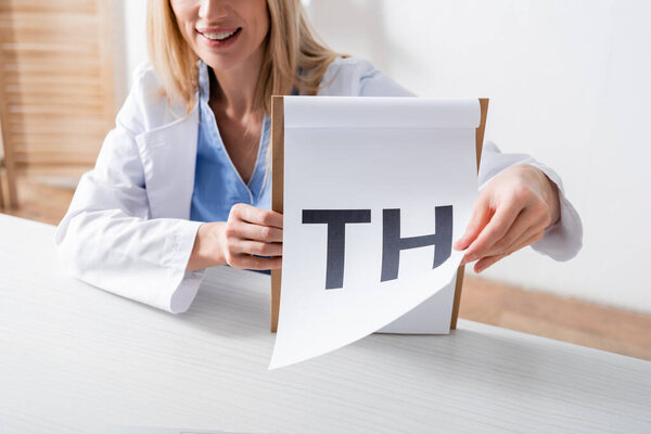 Cropped view of smiling speech therapist holding clipboard with letters in consulting room 