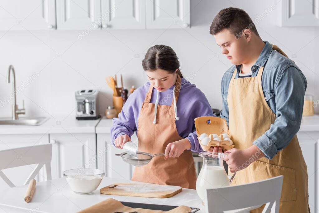 Teenagers with down syndrome cooking near milk and flour in kitchen 