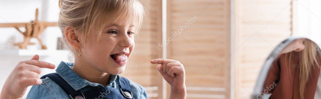 Child pointing with fingers while talking near blurred mirror during speech therapy in classroom, banner 