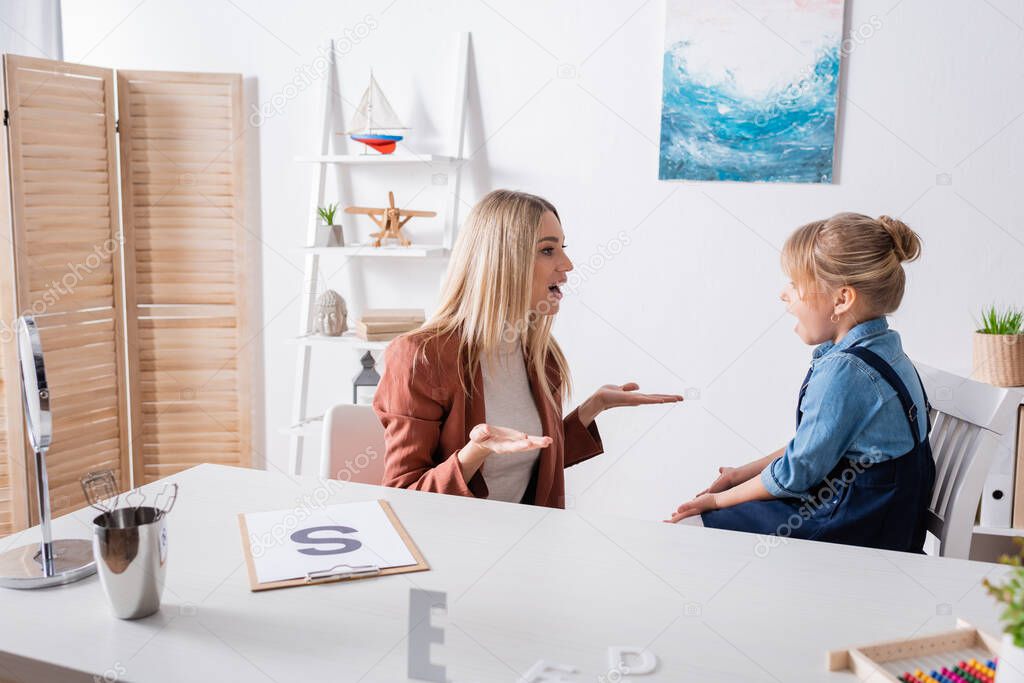 Speech therapist talking during lesson with girl in consulting room 