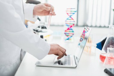 Laboratuvarda dizüstü bilgisayarı kullanarak genetik uzmanının test tüpüyle görüntülenmesi