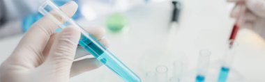 Lateks eldivenli bir bilim adamının mavi sıvı ve pankartla test tüpünü tutuşu kısmi görüntüsü