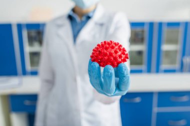 Kırmızı koronavirüs bakteri modelinin seçici odağı bulanık arka plandaki kırpılmış bilim adamının elinde.