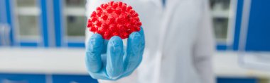 cropped view of blurred virologist holding red coronavirus bacteria model, banner clipart