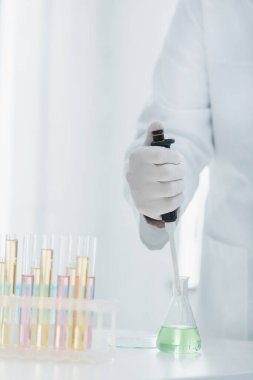 Lateks eldivenli genetikçinin, matara ve test tüplerinin yanında mikropipet tutarken kısmi görüntüsü