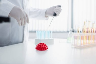 Kırmızı koronavirüs bakteri modelinin yanında çalışan bulanık virüs uzmanının kısmi görüntüsü