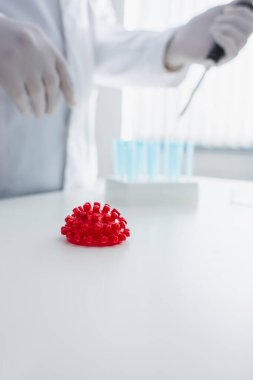 Kırmızı koronavirüs bakteri modelinin seçici odağı bulanık arka planda kırpılmış bilim adamının yanında.