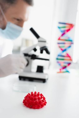Kırmızı koronavirüs bakteri modelinin seçici odak noktası bulanık arka planda tıbbi maskeli virüs uzmanı