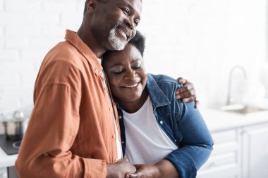 Mutlu ve yaşlı Afrikalı Amerikalı çift el ele tutuşuyor ve evde sarılıyorlar.