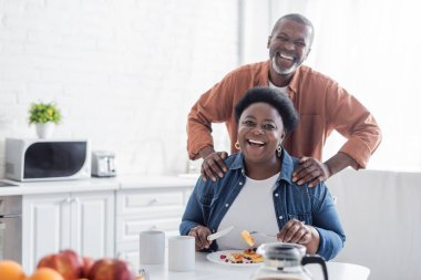 Mutlu ve kıdemli Afrikalı Amerikalı adam kahvaltı sırasında karısının arkasında duruyor. 