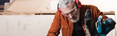 middle aged carpenter working near miter saw in workshop, banner clipart