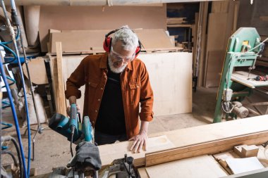 middle aged woodworker cutting timber in carpentry studio clipart