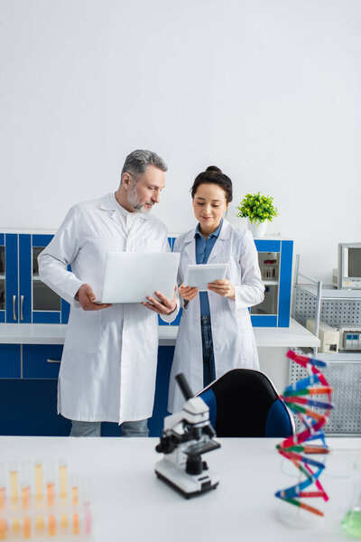 scientists in white coats standing with laptop and digital tablet in lab