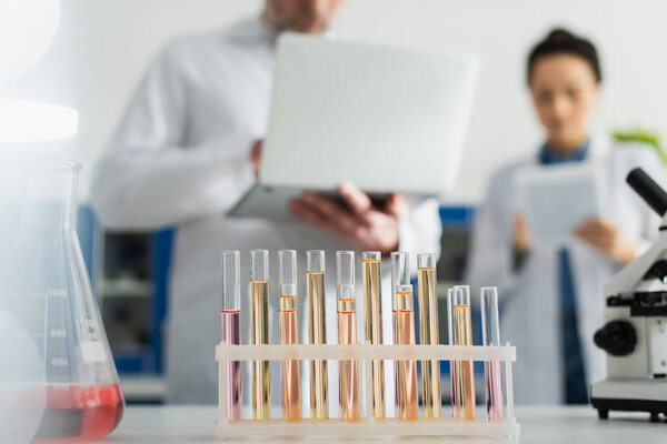 selective focus of test tubes near scientists with gadgets on blurred background